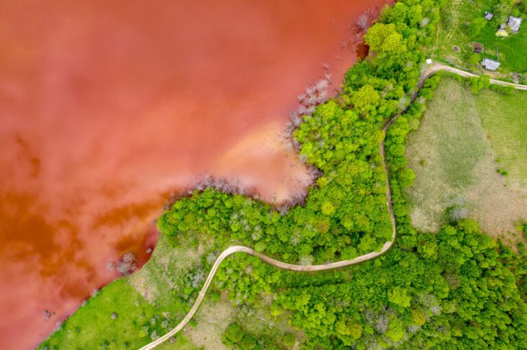 Aerial view of colorful red copper mining waste water in contrast with fresh green forest by drone