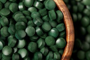 close up view of wooden bowl with pile of spirulina pills