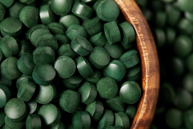 close up view of wooden bowl with pile of spirulina pills