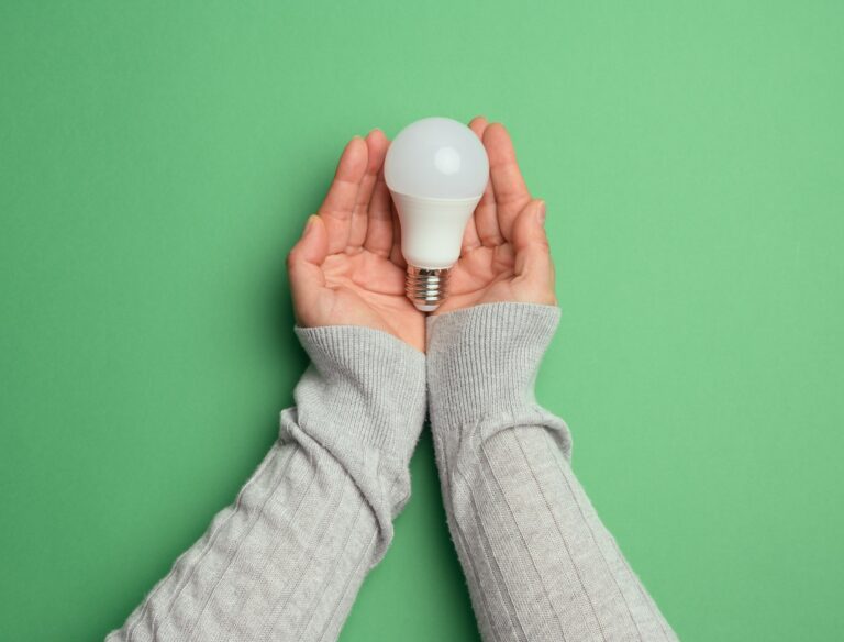 Female hands holding white glass lamp, green energy